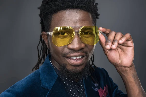 Handsome african american man in yellow sunglasses looking at camera isolated on gray — Free Stock Photo