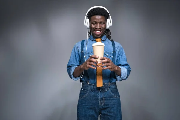 Szczęśliwy człowiek african american słuchanie muzyki i trzyma kawę iść na szaro — Darmowe zdjęcie stockowe