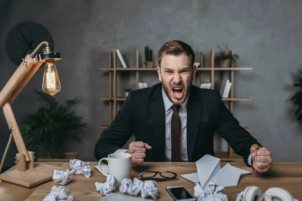 Hombre de negocios enojado gritando mientras está sentado en el lugar de trabajo - foto de stock