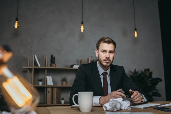 Jeune homme d'affaires en costume assis sur le lieu de travail — Photo de stock