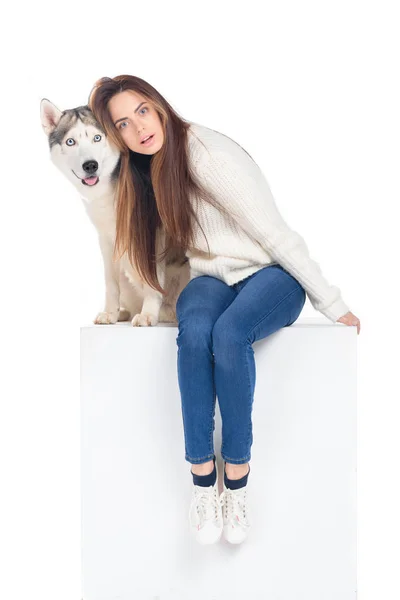 Красива здивована дівчина сидить на білому кубі з чоловічим собакою, ізольована на білому — стокове фото