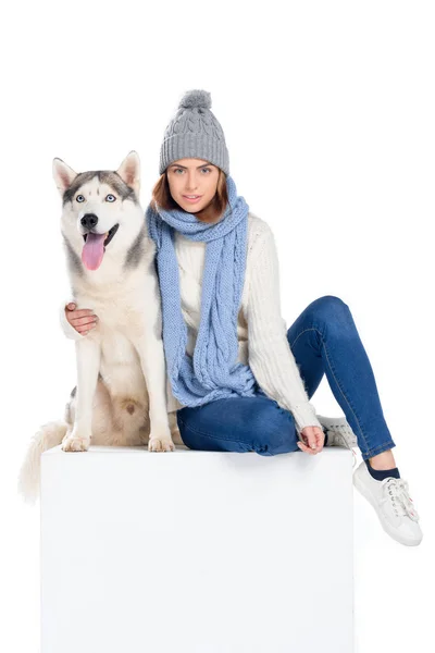 Husky dog and woman in knitted hat and scarf sitting on white cube, isolated on white — Stock Photo