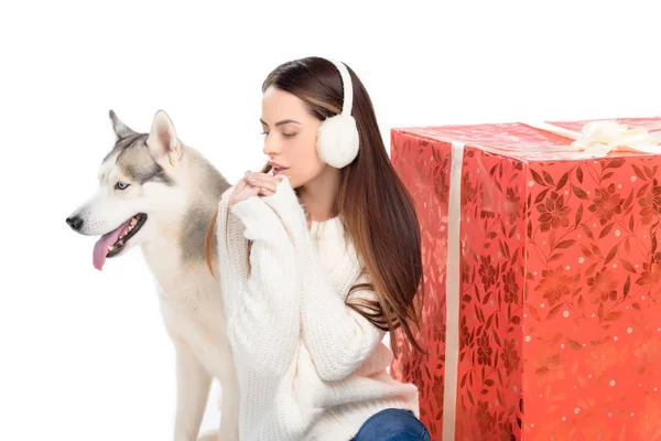 Husky dog and tender woman in winter earmuffs with big christmas gift behind, isolated on white — Stock Photo