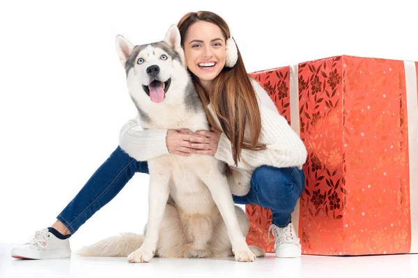 Cão husky e mulher rindo em earmuffs de inverno com grande presente de Natal atrás, isolado em branco — Fotografia de Stock