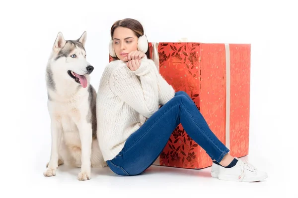 Husky-Hund und attraktive Frau im Winter-Ohrenschützer mit großem Weihnachtsgeschenk im Rücken, isoliert auf weiß — Stockfoto