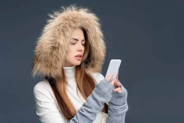 Mulher atraente em chapéu de pele usando smartphone, isolado em cinza — Fotografia de Stock