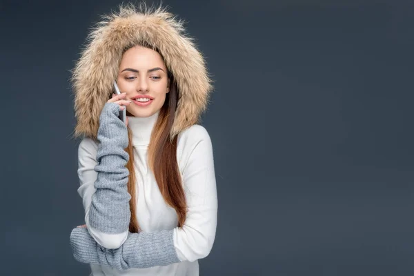 Улыбающаяся женщина в меховой шапке говорит смартфон, изолированный на серый — стоковое фото