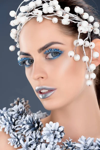 Attraktives Modell mit Haarschmuck, Tannenzapfen, Winter-Make-up und Glitzer, isoliert auf grau — Stockfoto