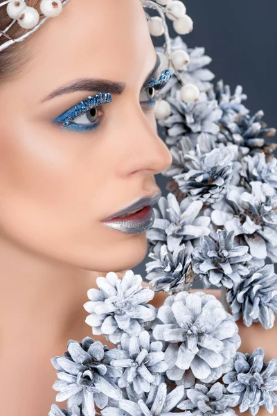 Hermosa mujer con conos de pino de Navidad, maquillaje de invierno y brillo, aislado en gris - foto de stock