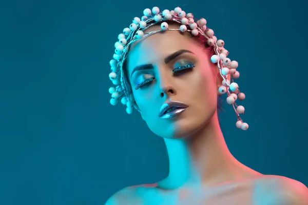 Retrato de mujer hermosa con accesorio para el cabello, maquillaje de invierno y purpurina posando para la sesión de moda, aislado en azul - foto de stock