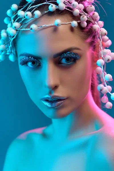 Portrait of attractive model with hair accessory, winter makeup and glitter posing for fashion shoot, isolated on blue — Stock Photo