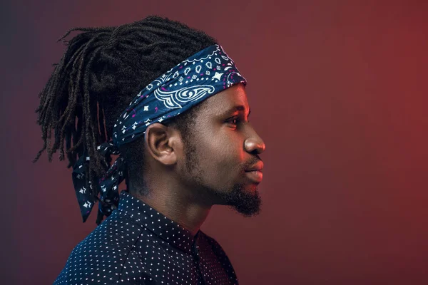 Side view of handsome african american man in headband isolated on burgundy — Stock Photo