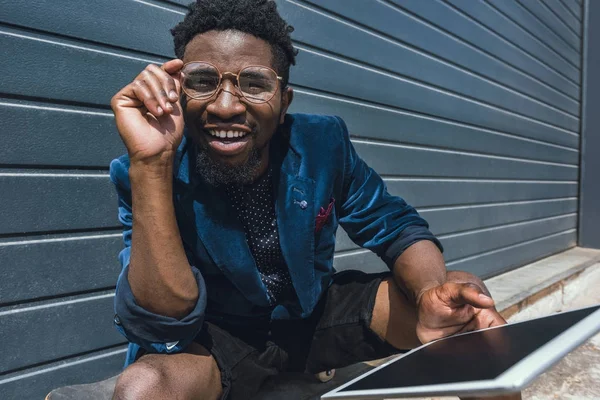 Sorrindo elegante homem americano africano em azul jaqueta segurando tablet e olhando para a câmera — Fotografia de Stock