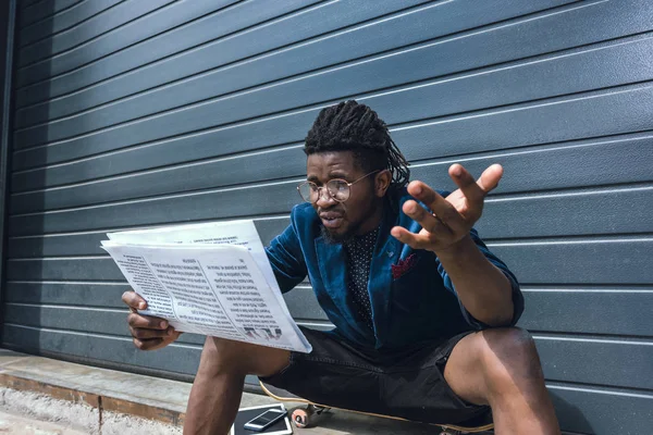 Choqué élégant homme afro-américain en veste bleue lecture journal — Photo de stock