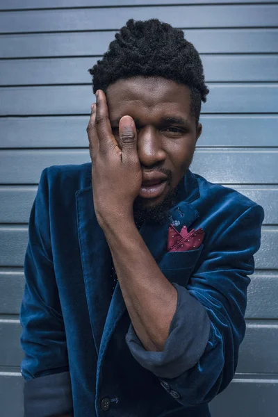 Hombre afroamericano con estilo en chaqueta azul que cubre el ojo con la mano - foto de stock