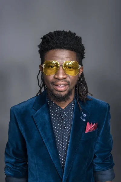 Hombre afroamericano guapo en gafas de sol amarillas y chaqueta azul aislado en gris - foto de stock