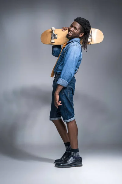 Souriant homme afro-américain à la mode avec patin sur l'épaule sur gris — Photo de stock