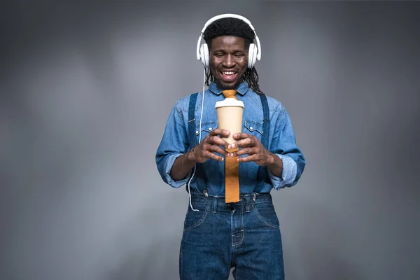 Homem americano africano feliz ouvindo música e segurando café para ir em cinza — Fotografia de Stock