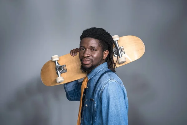 Homem americano africano na moda com skate no ombro em cinza — Fotografia de Stock