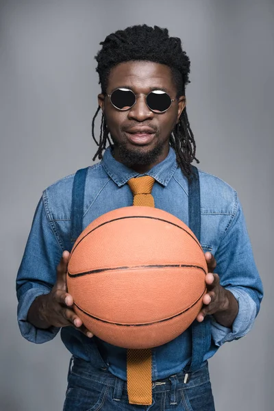 Schöner afrikanisch-amerikanischer Mann mit schwarzer Sonnenbrille hält Basketballball isoliert auf grau — Stockfoto
