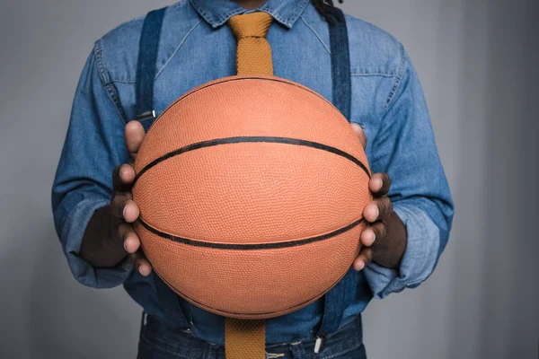 Imagen recortada de hombre afroamericano sosteniendo pelota de baloncesto aislado en gris - foto de stock