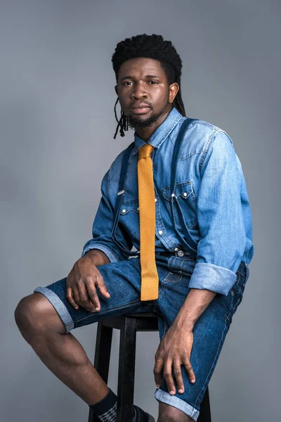 Bel homme afro-américain assis sur une chaise isolé sur gris — Photo de stock