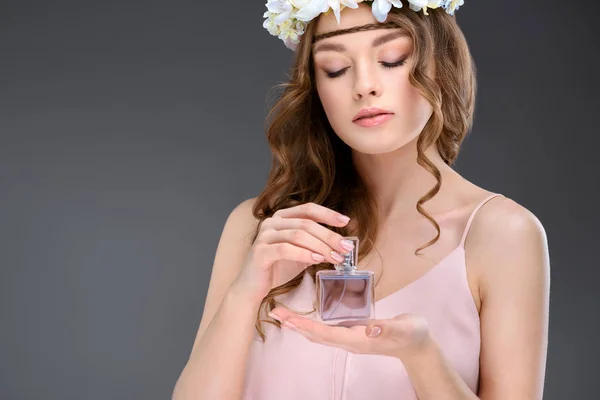 Attractive young woman in floral wreath smelling perfume isolated on grey — Stock Photo