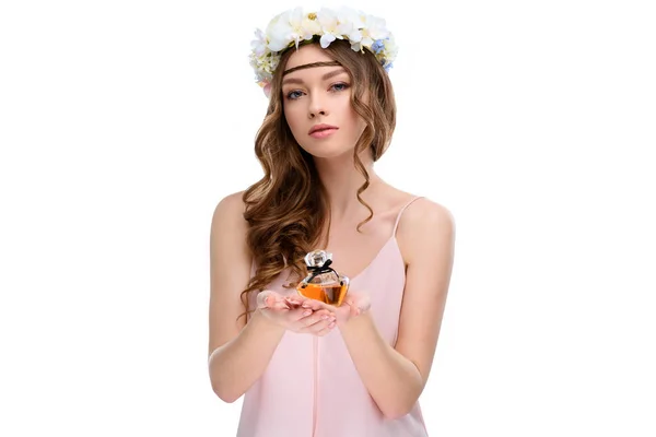 Hermosa joven en corona floral sosteniendo botella de perfume aislado en blanco - foto de stock