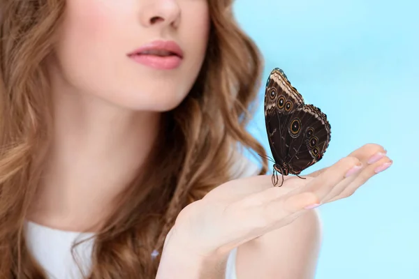 Обрізаний знімок красивої молодої жінки з метеликом на руці ізольовано на синьому — стокове фото