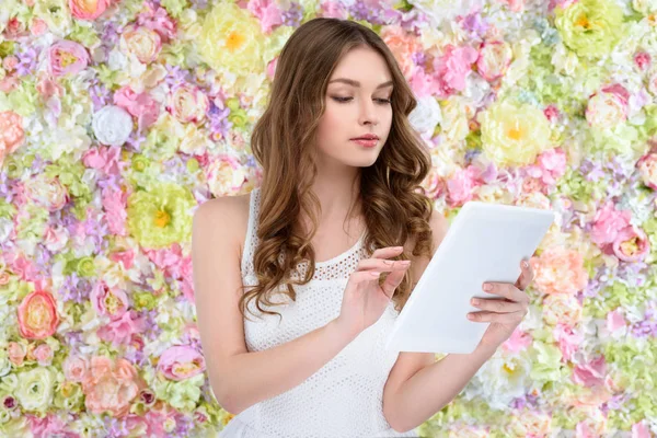 Bela jovem mulher usando tablet no fundo floral — Fotografia de Stock