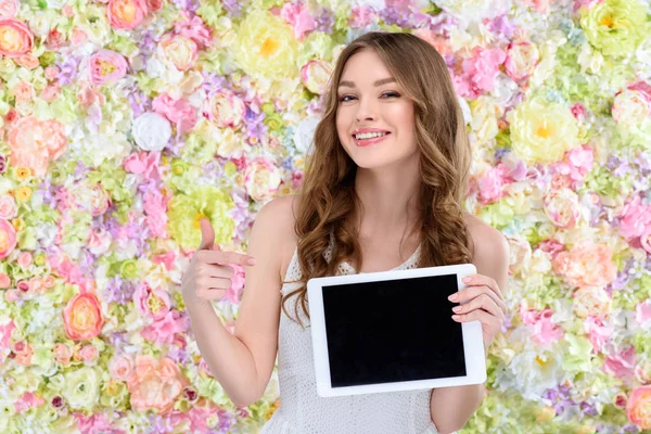 Belle jeune femme pointant vers la tablette sur fond floral — Photo de stock
