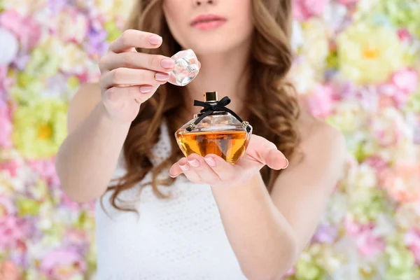 Tiro recortado de la mujer botella de apertura de perfume sobre fondo floral - foto de stock