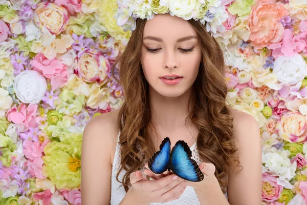 Atraente jovem mulher em coroa floral segurando borboleta azul — Fotografia de Stock