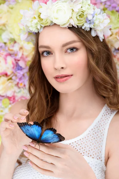Smiling young woman in floral wreath with butterfly on hand — Stock Photo