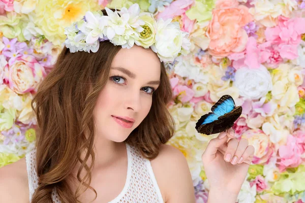 Mujer joven en corona floral con mariposa en la mano - foto de stock