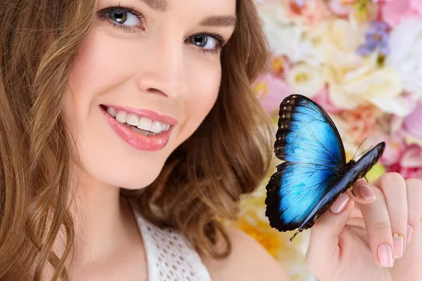 Крупным планом портрет улыбающейся молодой женщины с бабочкой на руке — стоковое фото