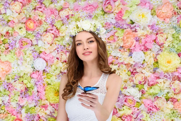 Hermosa joven en corona floral con mariposa en la mano - foto de stock