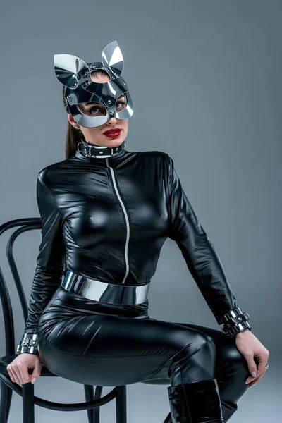 Привлекательная горячая девушка в костюме и маске позирует на стуле, изолированном от серых — стоковое фото