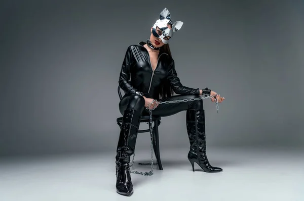 Kinky Frau in sexy Kostüm sitzt auf Stuhl und hält Kette auf grauem Hintergrund — Stockfoto