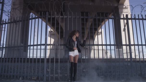 Mooi meisje blijven en poneren in de buurt van het hek onder de brug. Industriezone mode videoshoot — Stockvideo