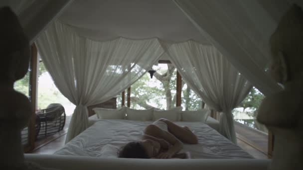 La ragazza addormentata si sveglia. Letto romantico sotto il baldacchino. Camera da letto nella foresta. La donna si allunga, sbadiglia e si sveglia a letto. Si sveglia e si alza rapidamente dal letto. Ho dormito troppo! Rallentatore — Video Stock