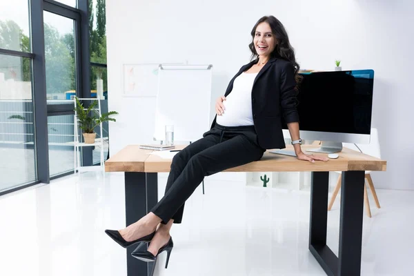 Schwangere Geschäftsfrau sitzt auf Arbeitstisch — Stockfoto
