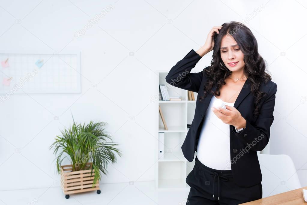 pregnant businesswoman with jar of pills