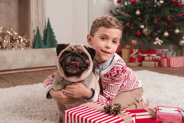 Мальчик обнимает мопса на Рождество — стоковое фото