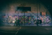 lidé drží kouřové bomby a stojí proti zdi s graffiti v noci