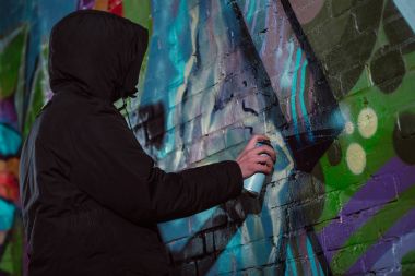 anonymous painting graffiti with aerosol paint on wall at night clipart