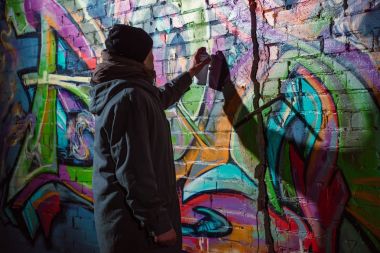street artist painting graffiti with aerosol paint on wall at night clipart