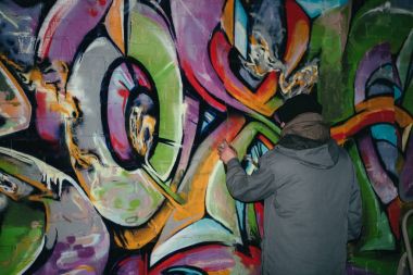 back view of street artist painting graffiti with aerosol paint on wall at night clipart