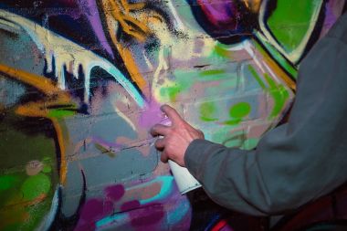 cropped view of street artist painting graffiti with aerosol paint on wall at night clipart