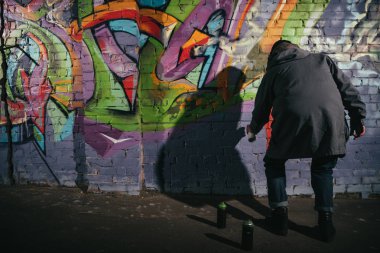rear view of street artist painting graffiti with aerosol paint on wall at night clipart